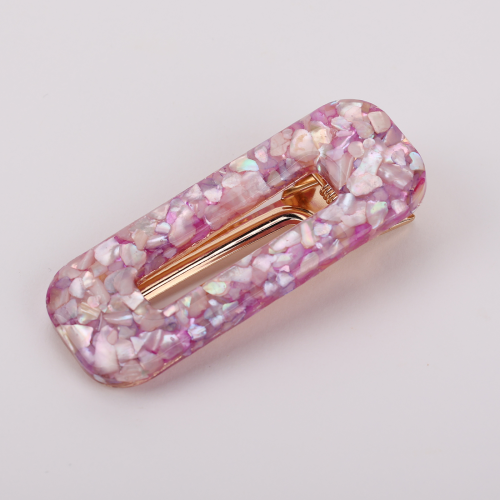 A pair of glossy resin snap hair clips in a pastel shell-inlay style, positioned as chic fashion hair accessories. One clip blends soft yellow, mint, and iridescent flecks with a silver-tone clasp, while the other features pink and lavender marbling with a warm gold-tone metal insert. Their rounded rectangular shape and luminous mosaic finish give them a feminine, polished feel suited to buyers drawn to playful elegance and boutique styling.
