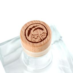 A clear square glass spirits bottle with a natural wooden cap, presented in a clean, minimalist premium style. The label is a striking dark panel with vivid blue line-art illustration and vertical Korean lettering, giving it an artisanal, contemporary edge. Its compact proportions, transparent glass, and restrained finish suggest a craft liquor or specialty soju aimed at design-conscious buyers. The overall mood is refined, modern, and gift-worthy.