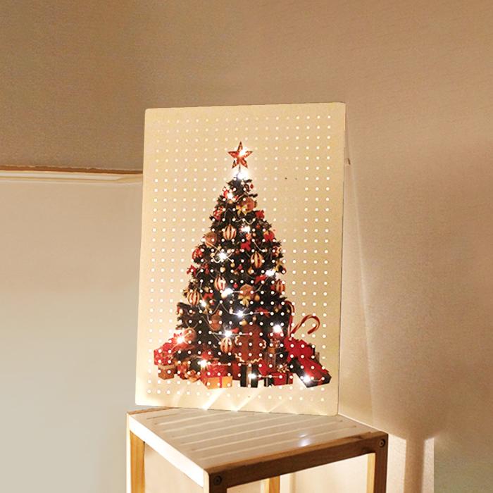 Pegboard printed with a Christmas tree design, decorated with LED lights, placed on a wooden stool for festive interior display