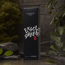 A sleek black rectangular cosmetic box for hair care, presented in a premium, minimalist style with bold graphic typography. The matte-looking surface is accented by white brushstroke lettering and a small red stamp-like mark, giving it an edgy, modern feel. Subtle silver text and the tall, slim proportions suggest a refined specialty treatment, while the dark stone setting creates a moody, luxe aesthetic for design-conscious buyers.